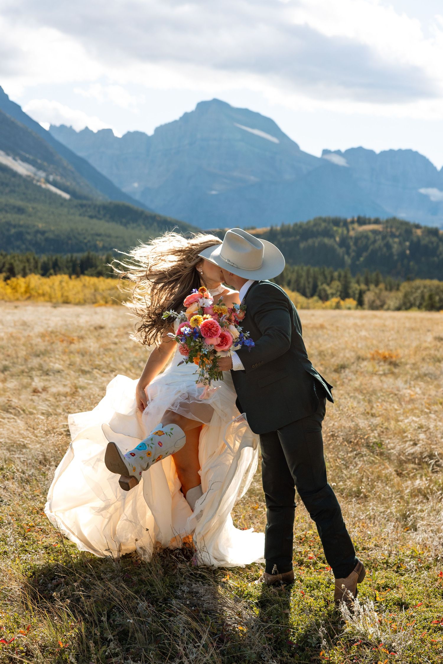 A romantic wedding photo in the mountains of Banff National Park with dramatic peaks and golden meadow in the background.