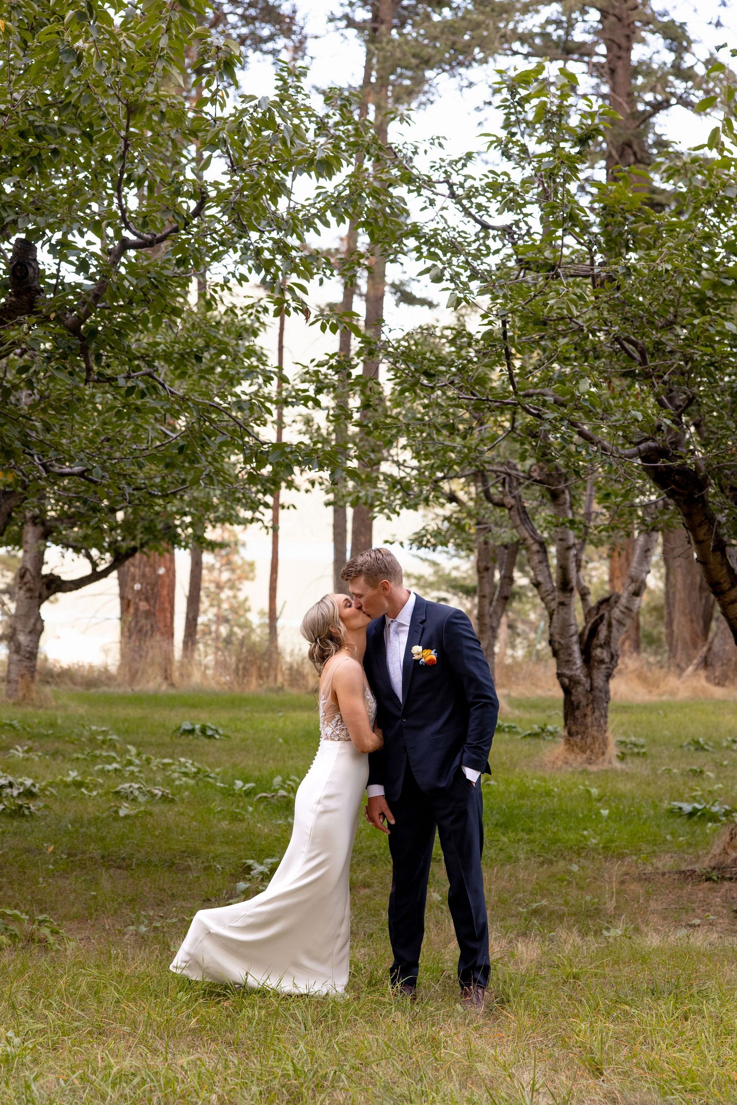 A romantic couple embraces among apple trees in an orchard setting during an outdoor wedding photo session.