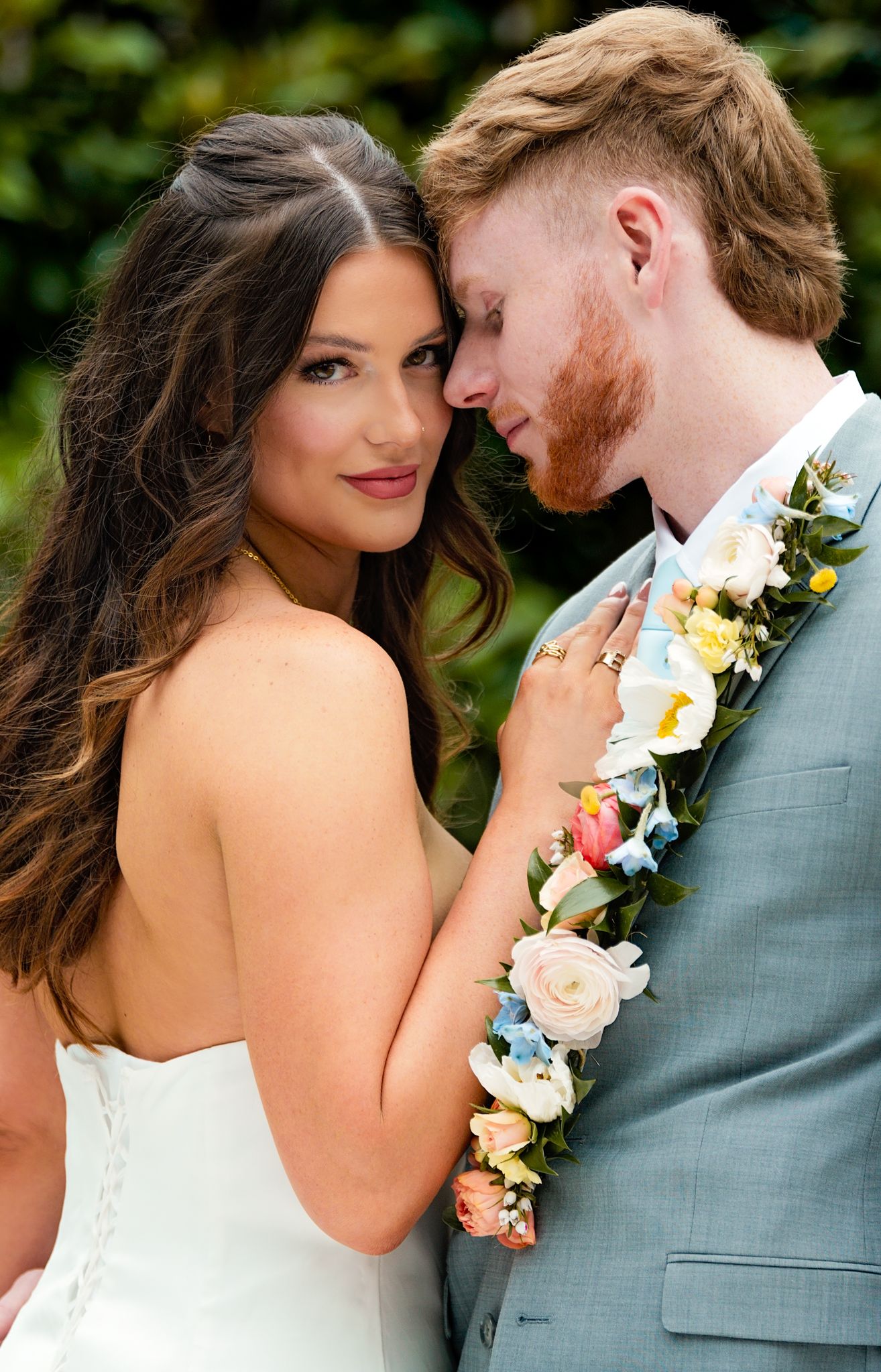Intimate portrait of newlywed couple with floral lei against garden background.
