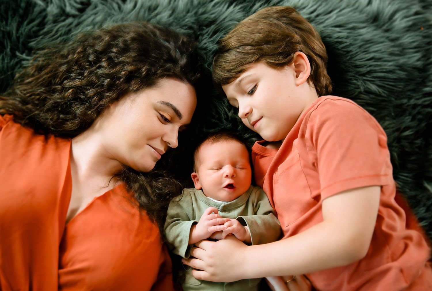 A tender family moment with two siblings cuddling their newborn baby on a plush surface.