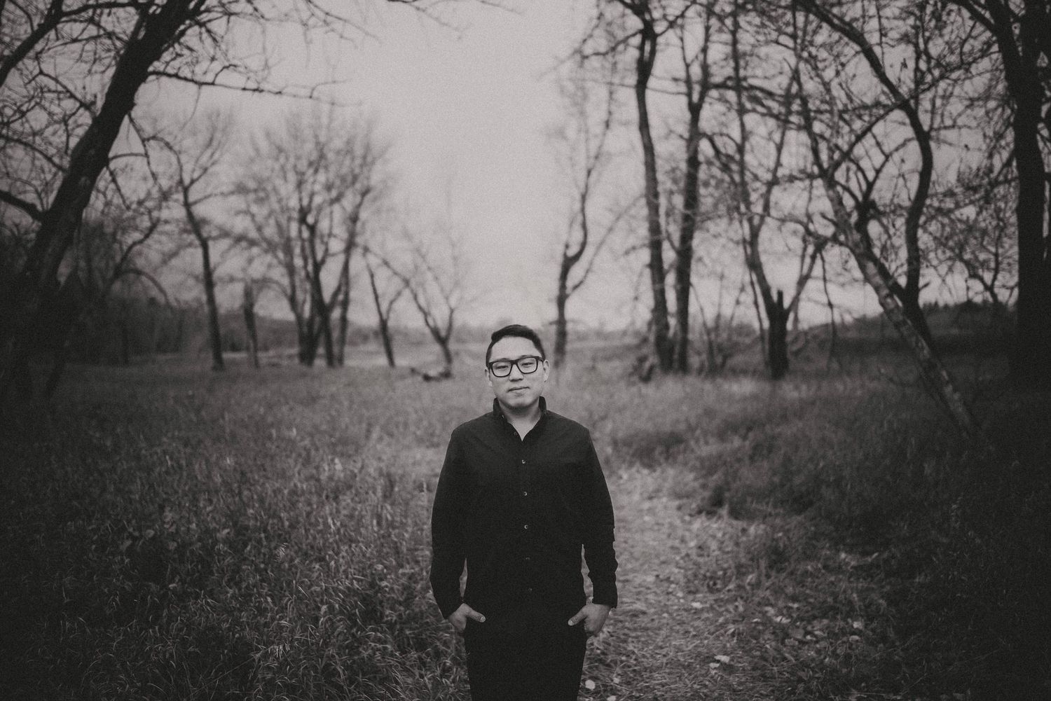 Black and white portrait in a winter field with bare trees in the background.
