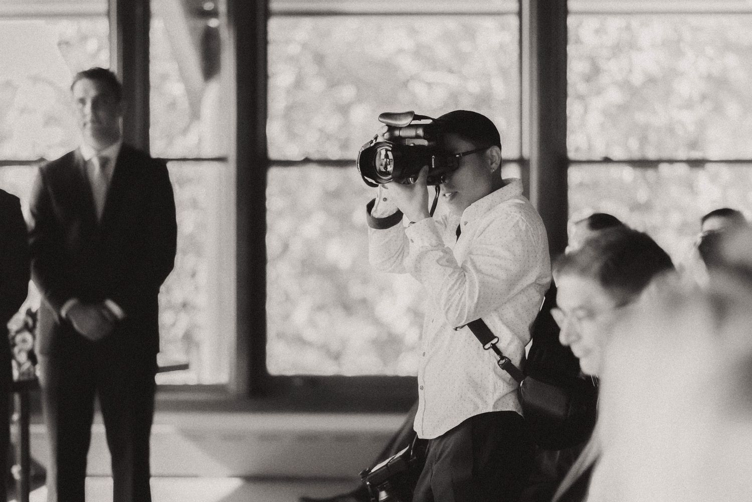 A photographer captures moments during an indoor event near large windows.