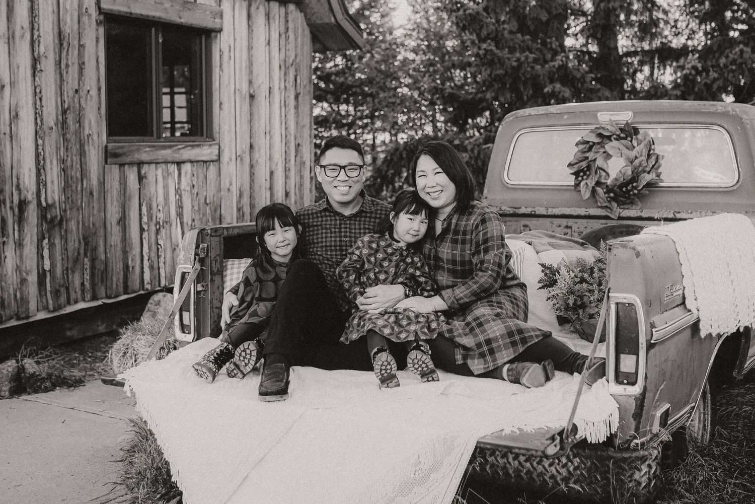 Vintage black and white photo of family members sitting on a classic truck bed.