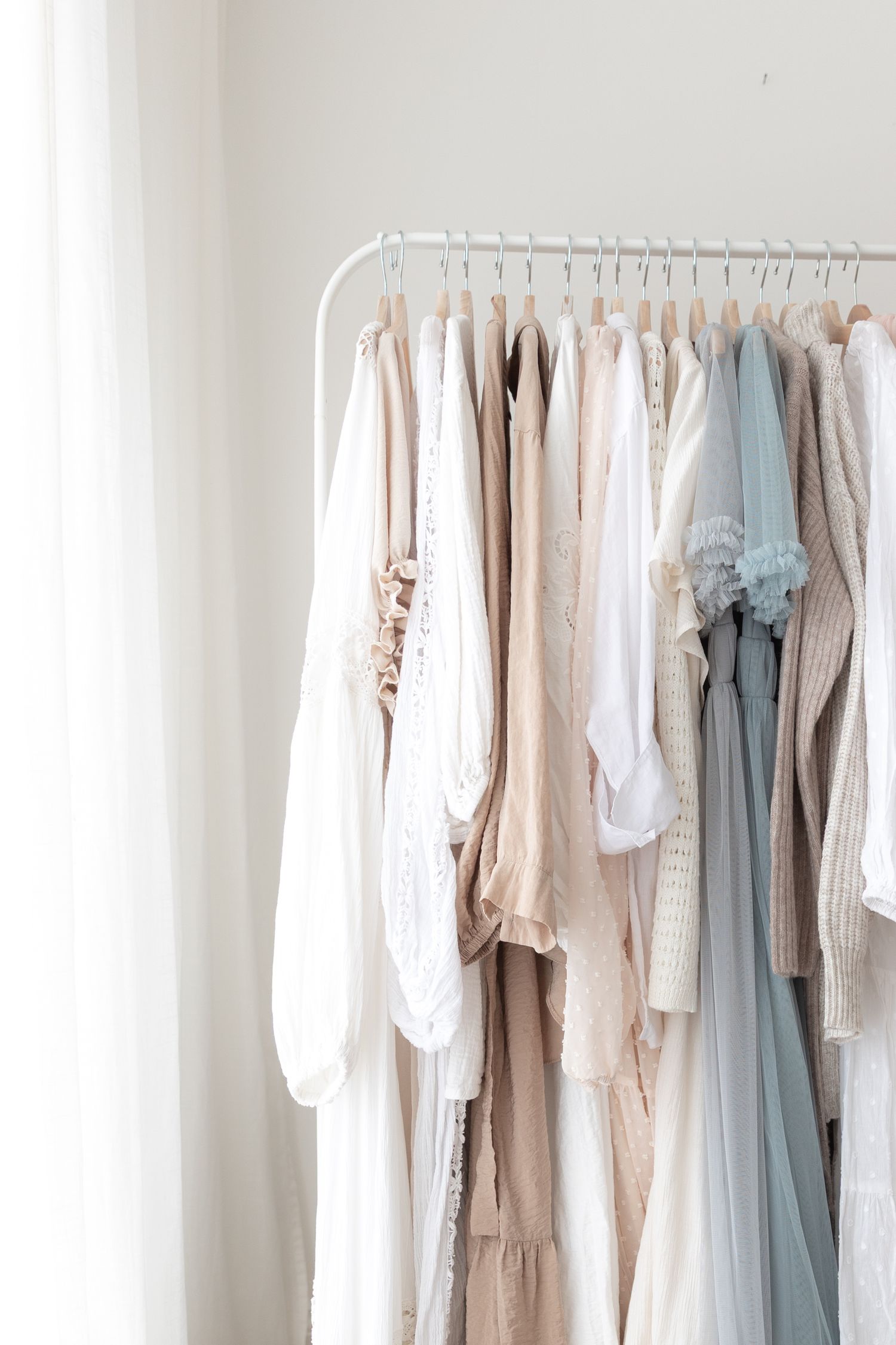 Soft pastel clothing hanging on white garment rack against neutral wall. Client Wardrobe