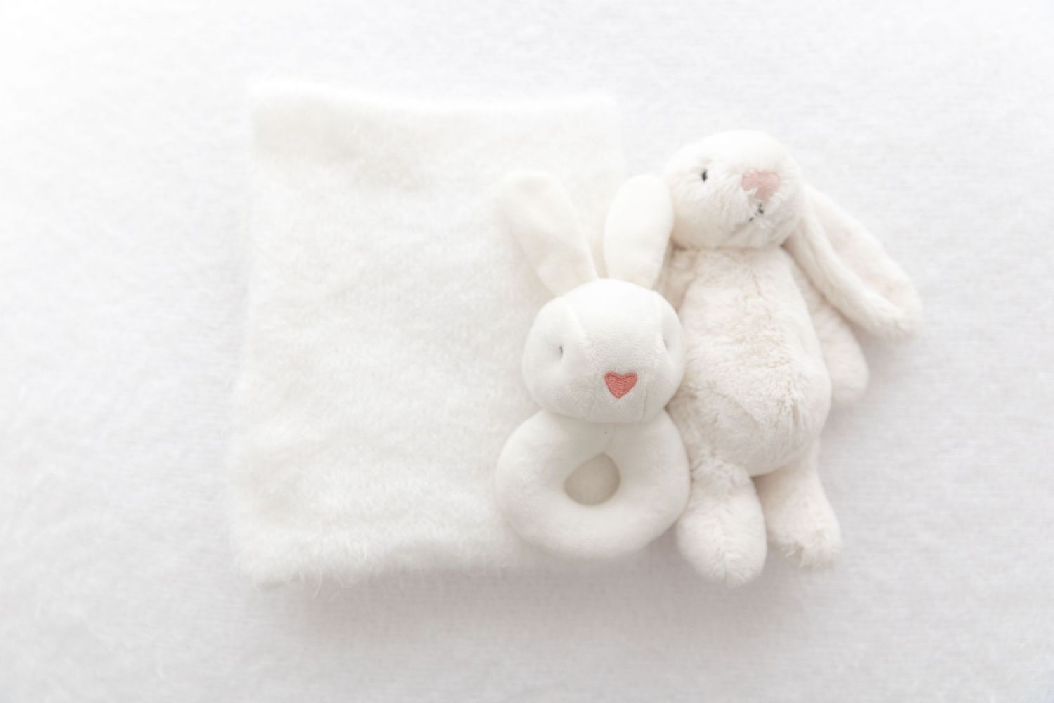 White plush bunny toy and rattle on soft white blanket against light background.