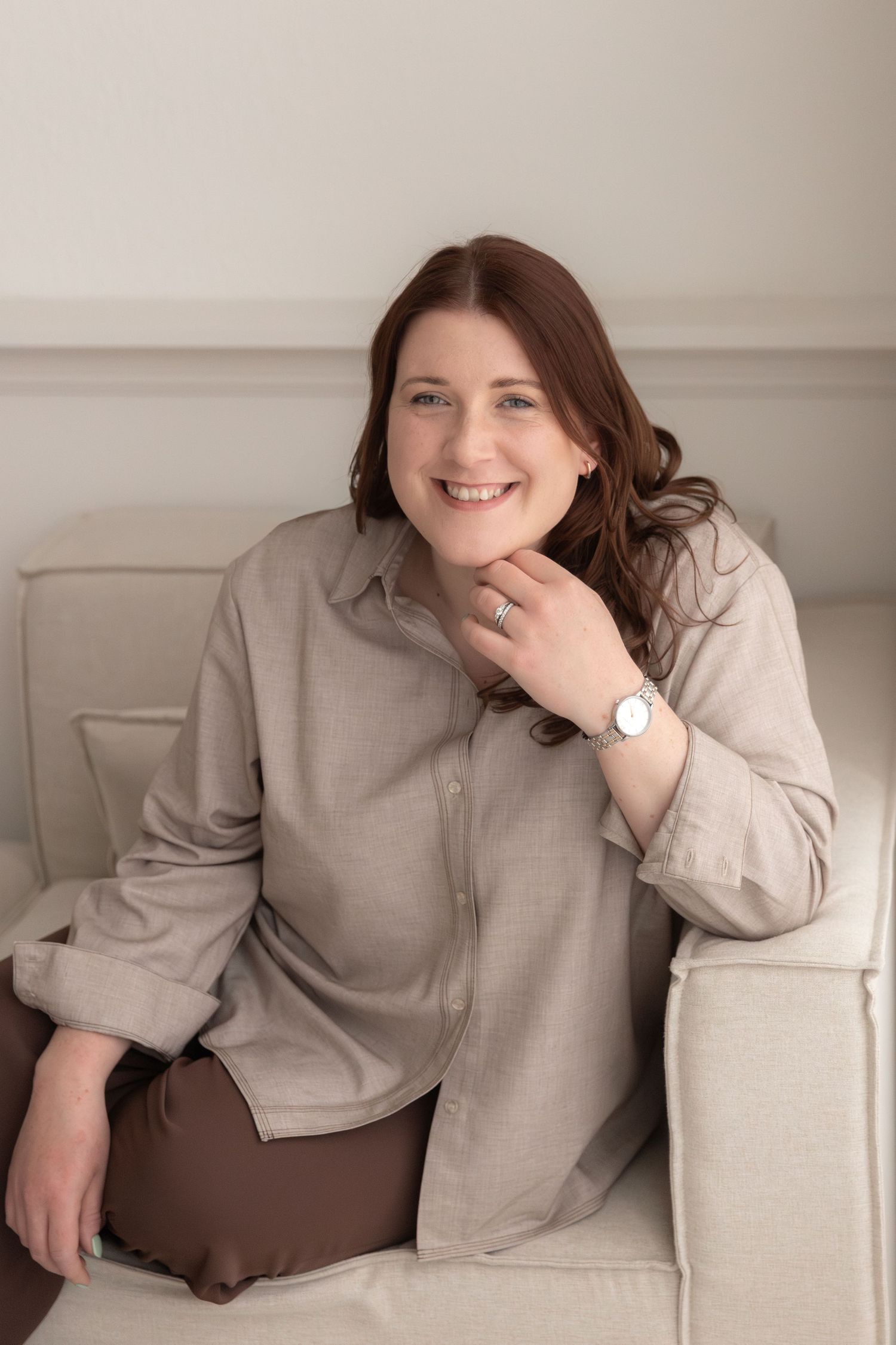 Professional portrait of someone in a beige button-down shirt sitting on a light colored couch.