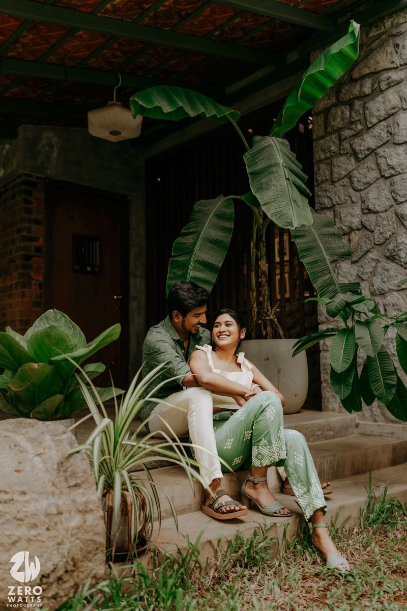 People sharing moments on stone steps surrounded by tropical plants and rustic brick wall decor.