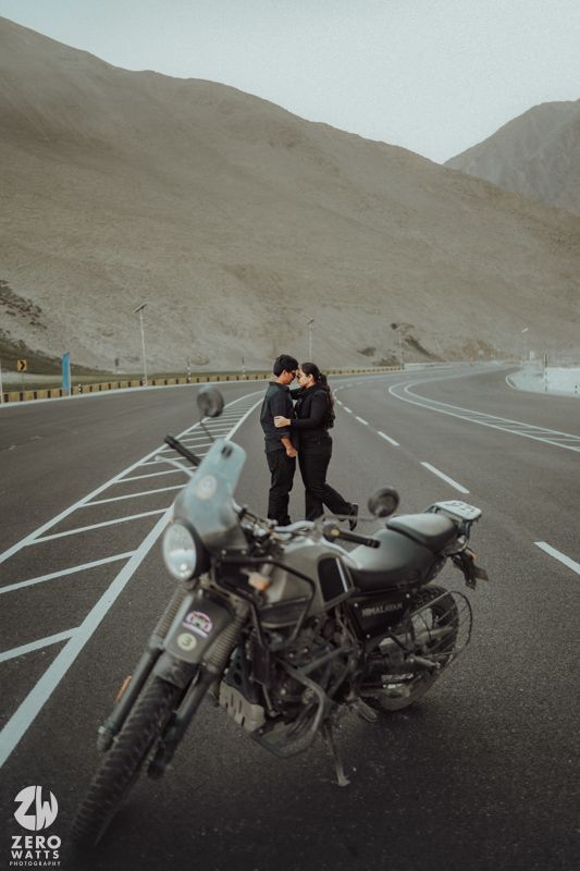 A motorcycle parked on a winding mountain road with barren hills in the background.