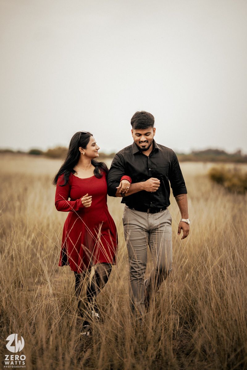 A couple sharing laughter while walking through tall grass in a field.