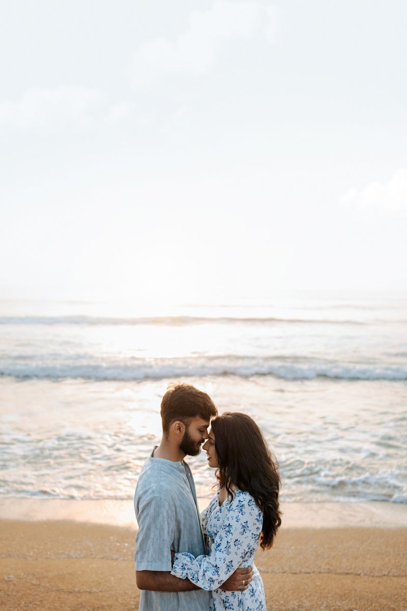 Romantic couple embracing on beach at sunset with ocean waves in background.
