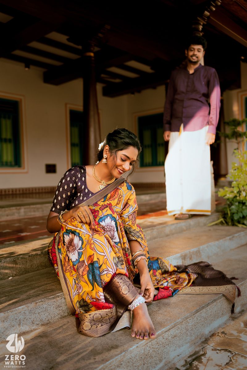 A scenic capture of traditional South Indian fashion with a person in vibrant printed saree seated on stone steps.