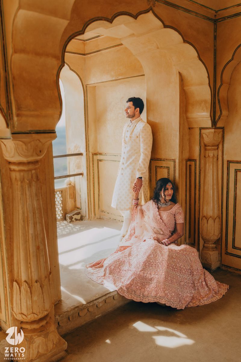 Couple in traditional Indian wedding attire pose in ornate archway during wedding photoshoot.
