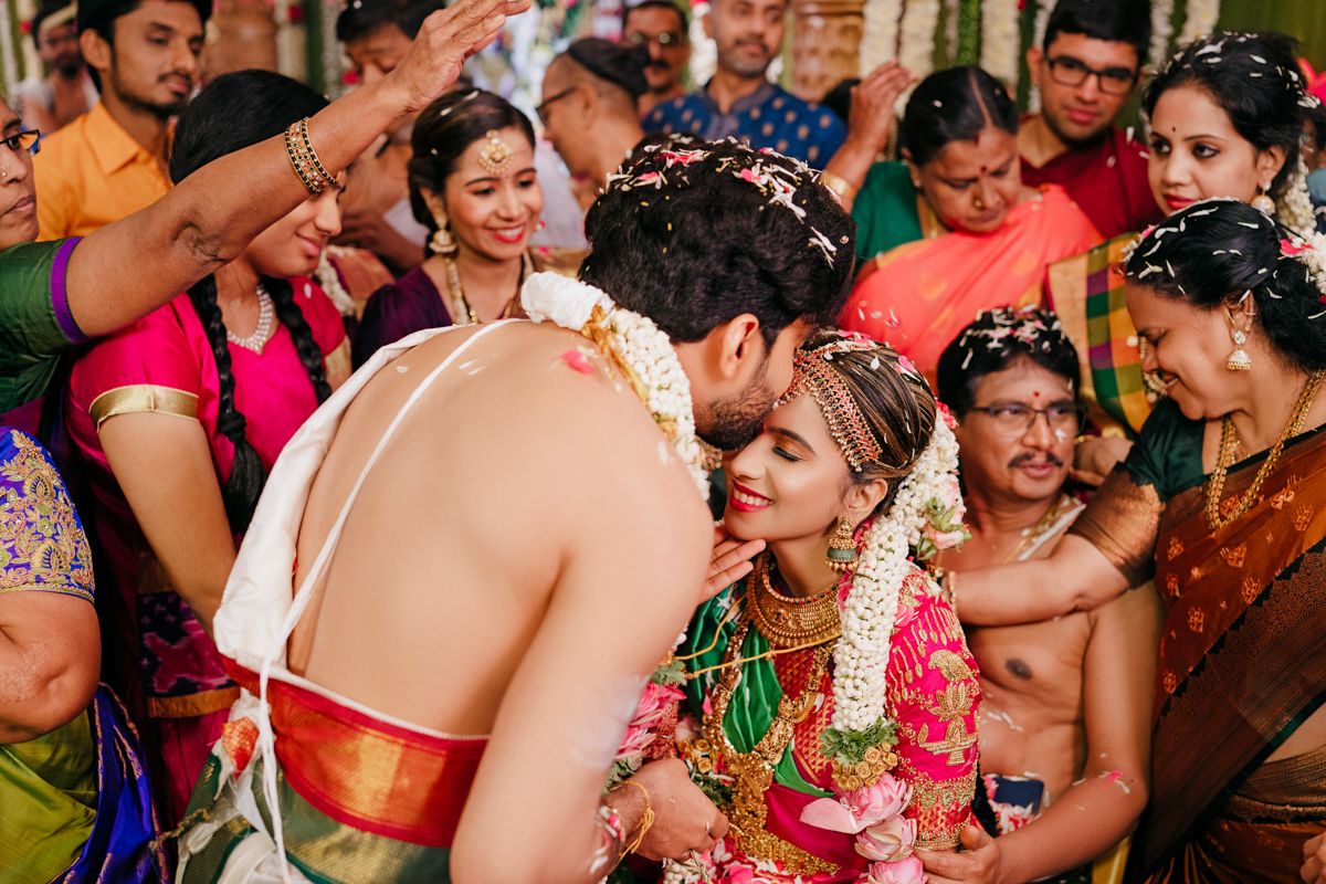 Traditional South Indian wedding celebration with a couple exchanging garlands surrounded by colorfully dressed guests.
