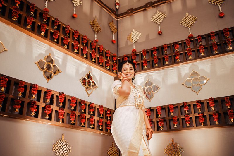 Traditional bride posing in white attire against wall decorated with red lanterns and golden ornaments.