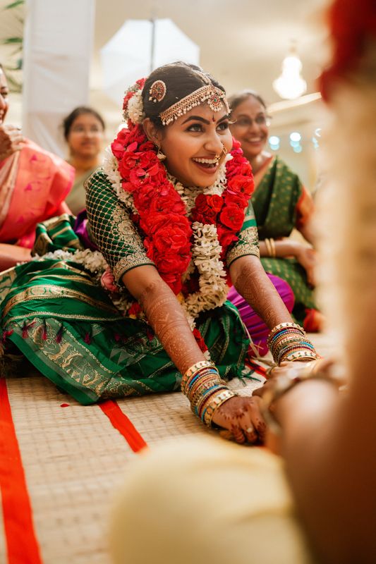 A bride wearing traditional South Indian wedding attire with red garlands and ornate jewelry smiles during the ceremony.
