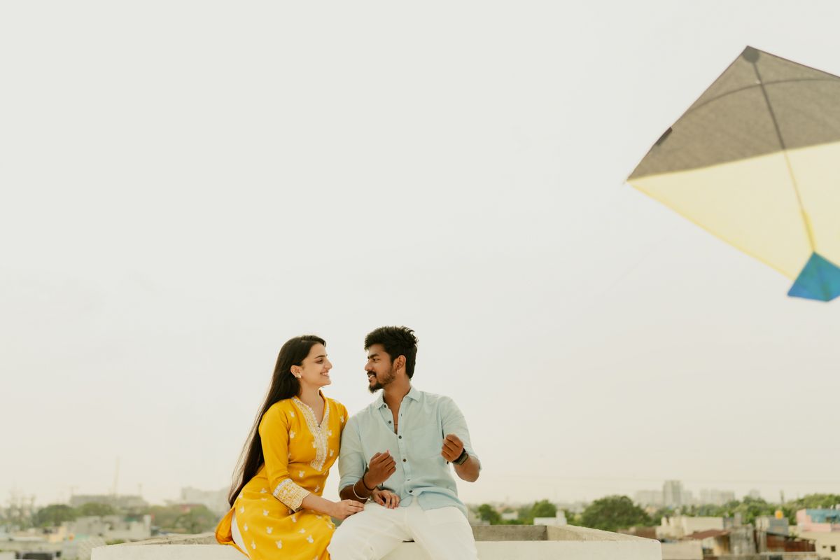 Two people in yellow and white outfits share a joyful moment while flying kites on an urban rooftop.