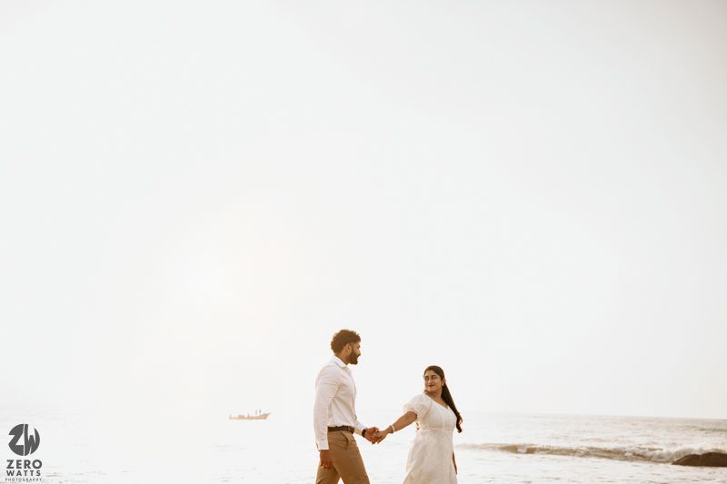 A couple in light colored outfits sharing an intimate moment on a misty beach.