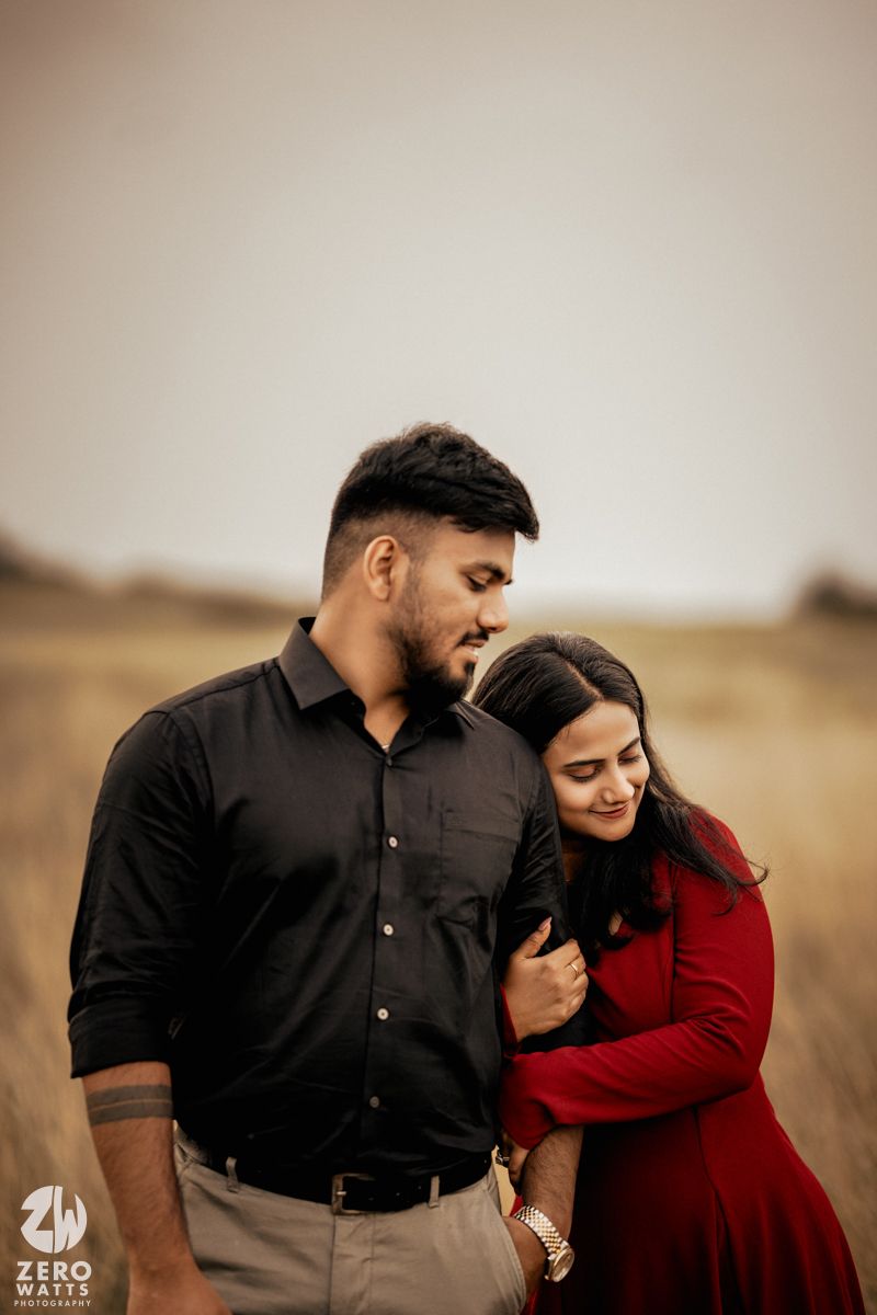 A couple embraces while standing in tall grass during golden hour wearing coordinated red and black outfits.