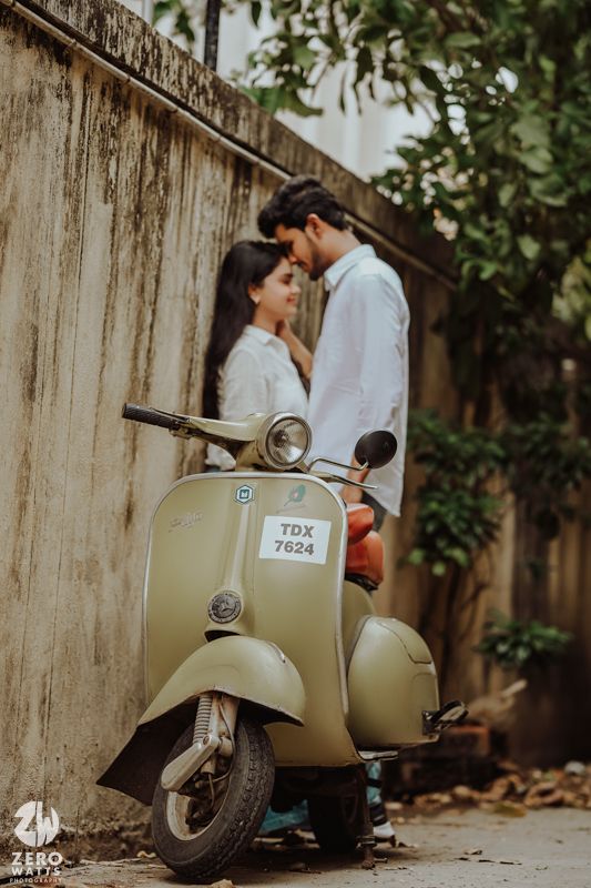 Romantic couple pose with vintage cream Vespa scooter against weathered wall.