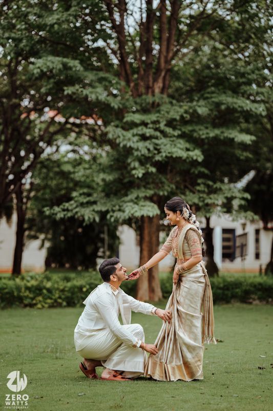 Couple in traditional Indian attire share a romantic moment on a lawn surrounded by lush green trees.