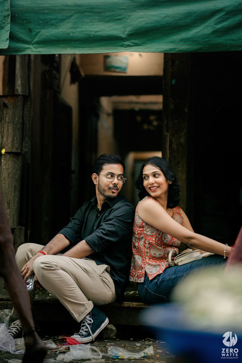 Couple sitting together and smiling under a green awning in a cozy alleyway setting.