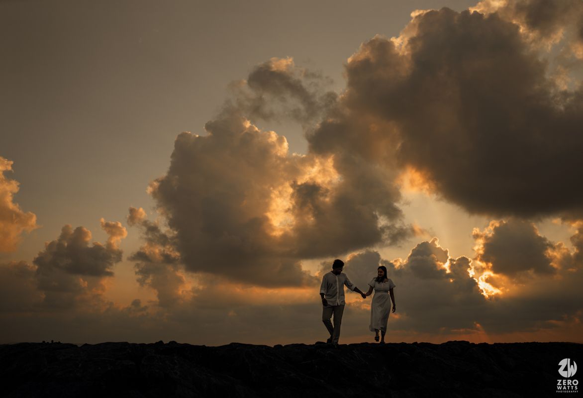 Silhouette of couple holding hands against dramatic sunset sky with clouds.