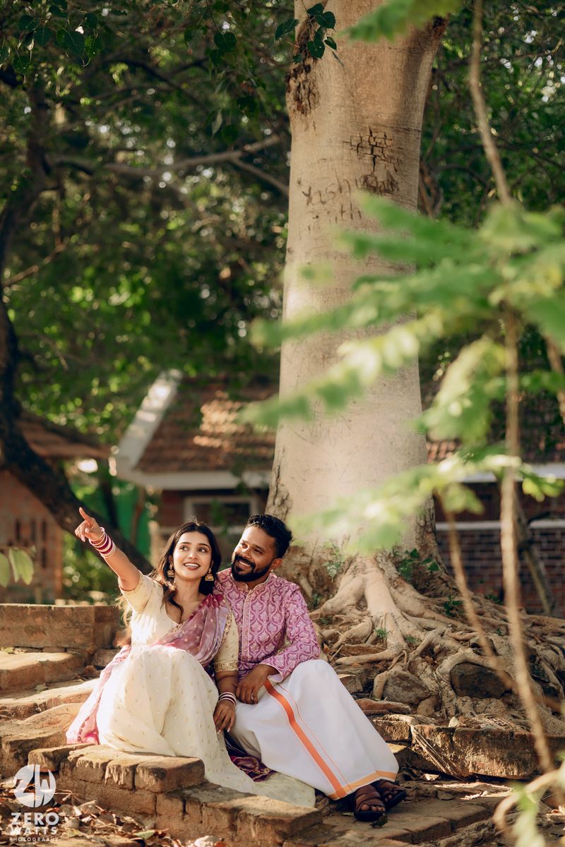 Couple sitting under a large tree trunk in traditional Indian clothing.