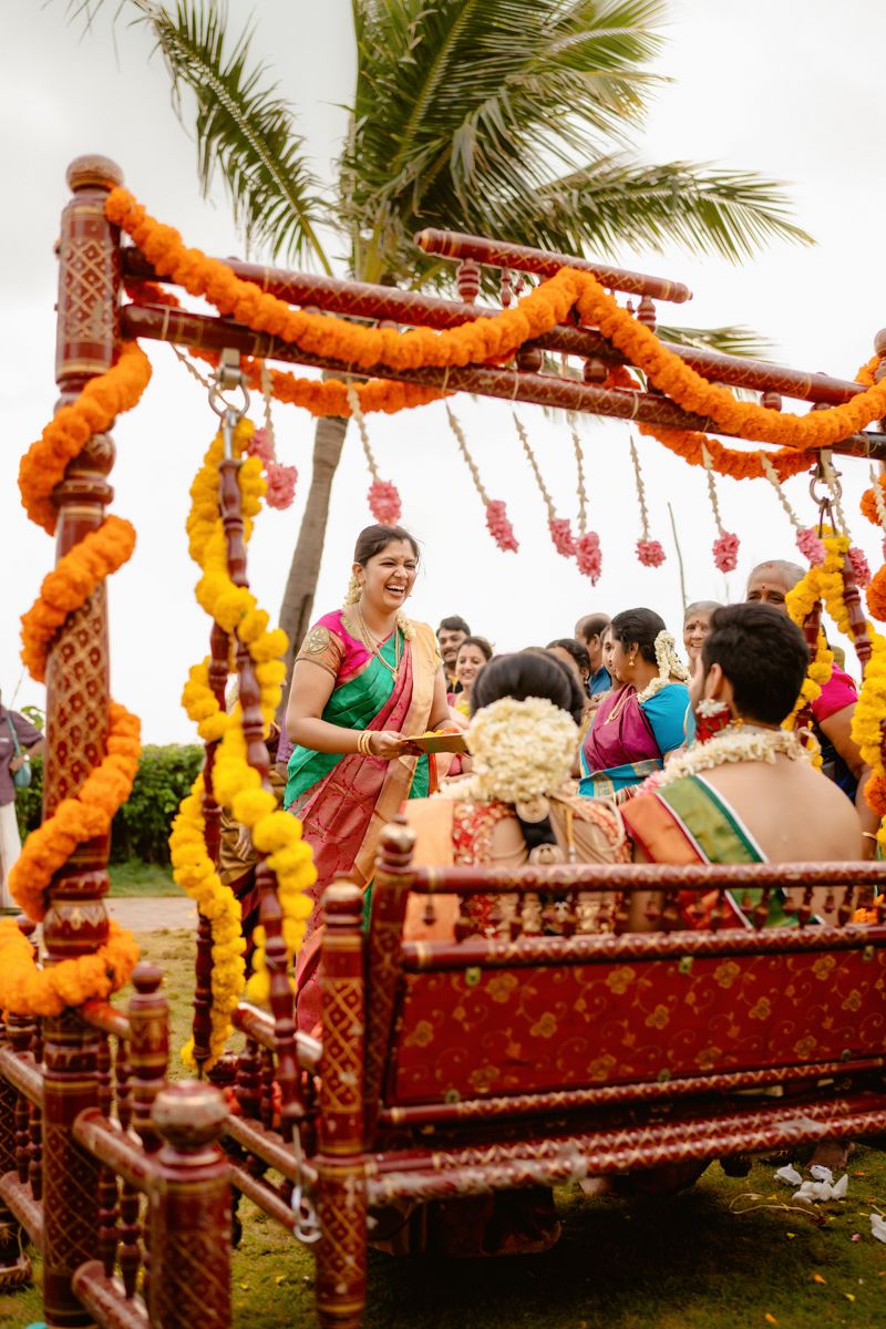 Decorated wedding swing with marigold garlands and palm trees in the background during an outdoor celebration.