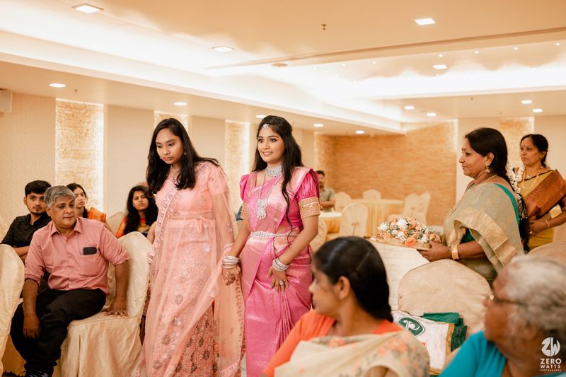 Guests in traditional Indian formal attire gather in an elegant banquet hall with warm lighting and cream-colored decor.