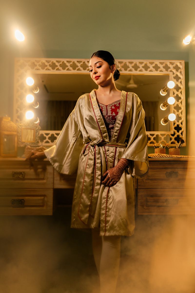 A soft-lit photo of someone wearing a luxurious gold silk robe in a dressing room with illuminated vanity lights.
