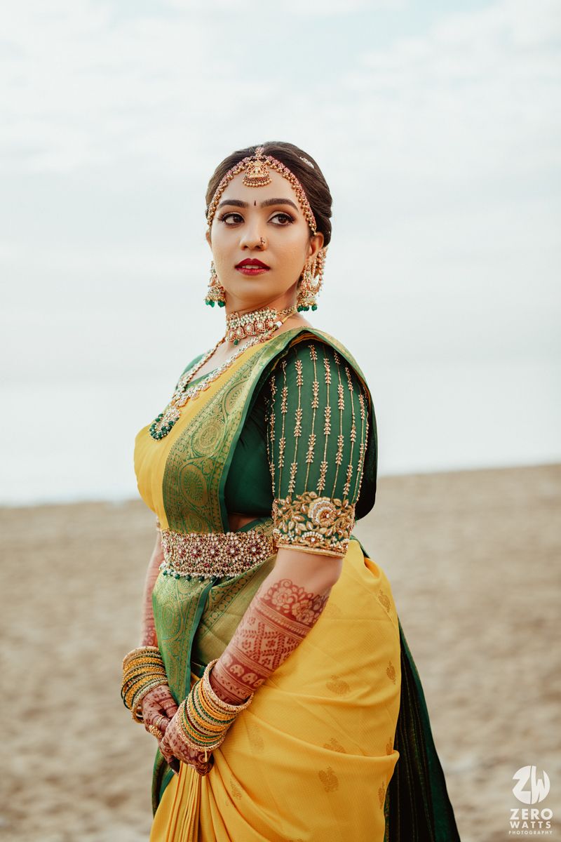 Traditional South Indian bride wearing yellow and green silk saree with ornate gold jewelry and embellishments at an outdoor setting.