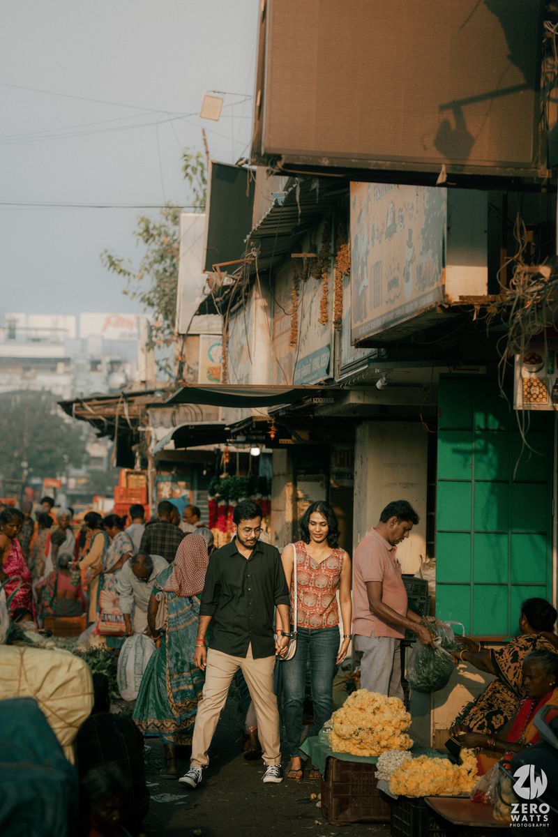 A couple exploring a bustling street market with colorful storefronts and vendors.