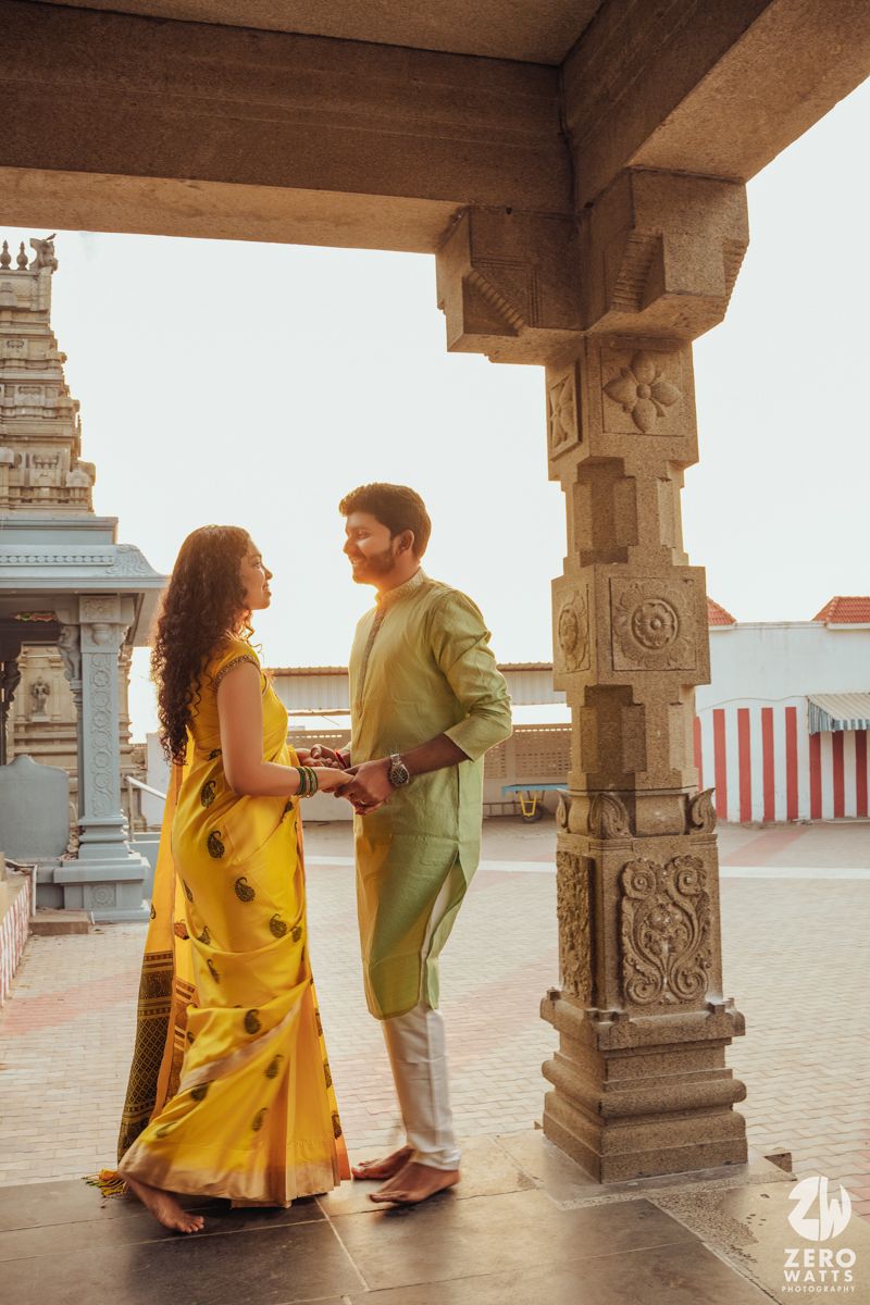 A couple standing together in traditional Indian attire under ornate temple architecture.