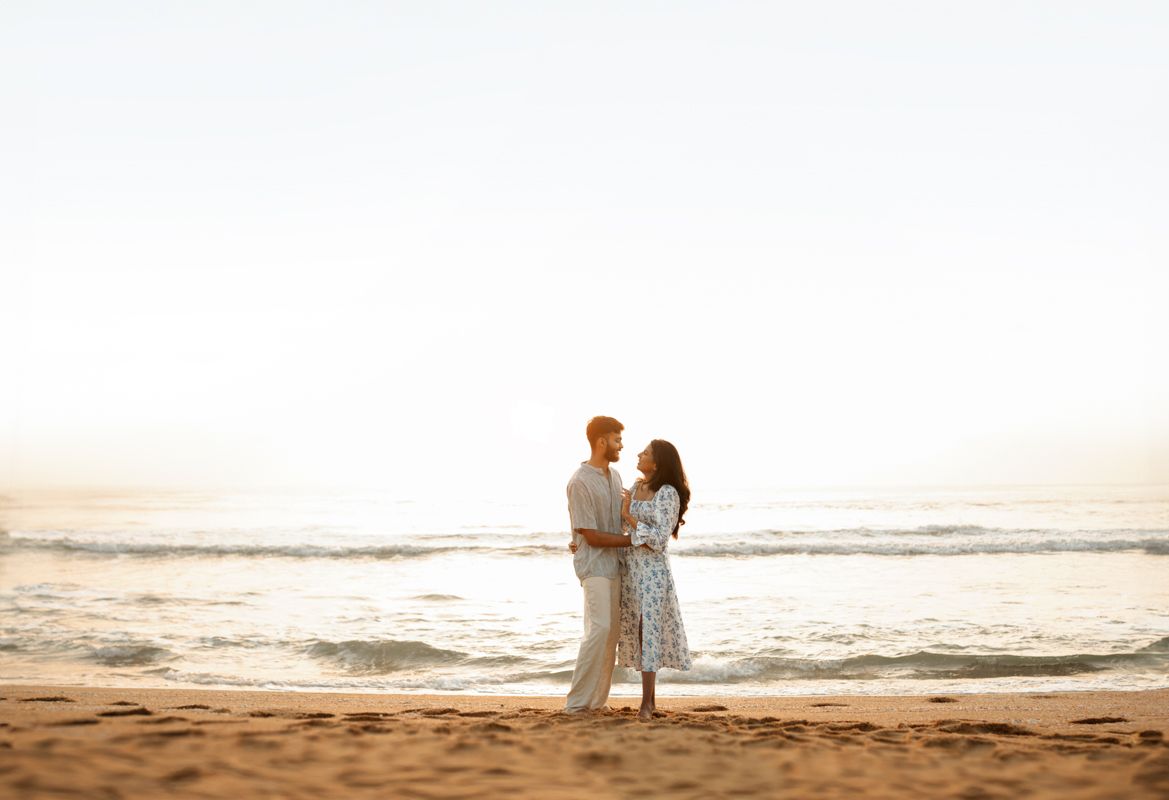 A couple embracing on a sandy beach during golden hour with waves in the background.