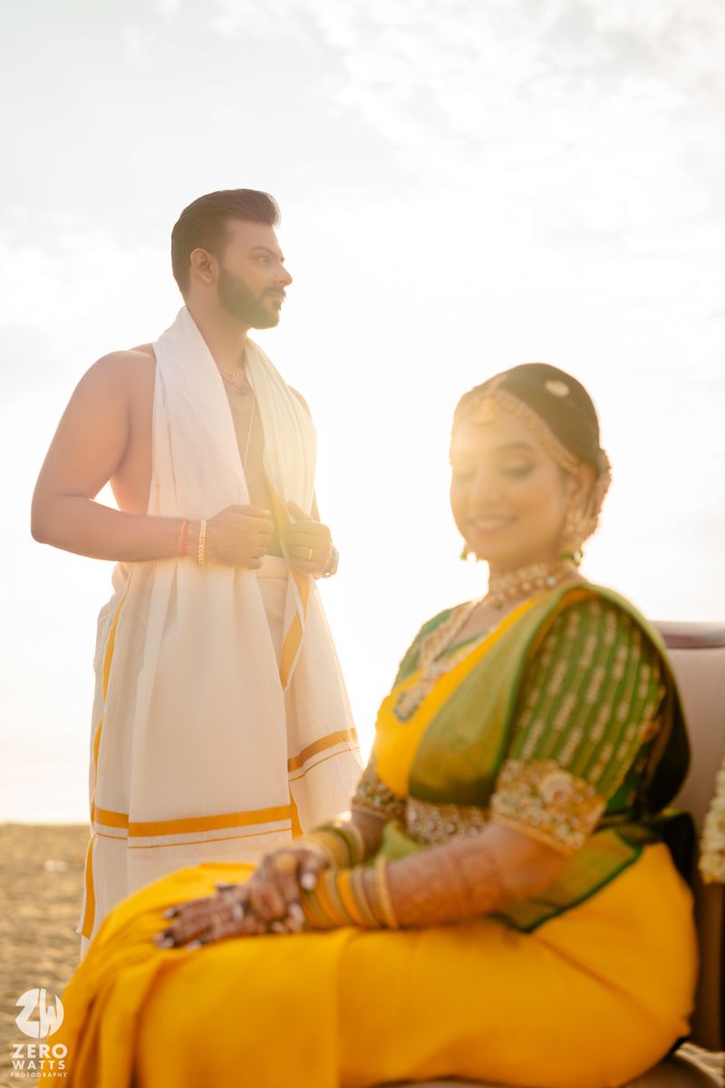 A couple in traditional South Indian attire poses at sunset, the person in yellow with henna-adorned hands and green patterned blouse.