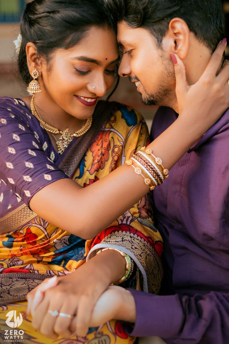 Traditional Indian couple shares intimate moment wearing purple and colorful ethnic attire with jewelry.