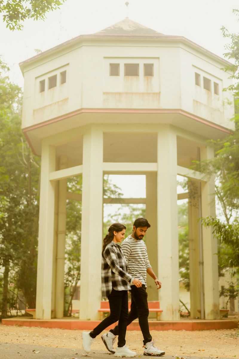 Couple walking together in front of a white gazebo structure in a park on a misty day.
