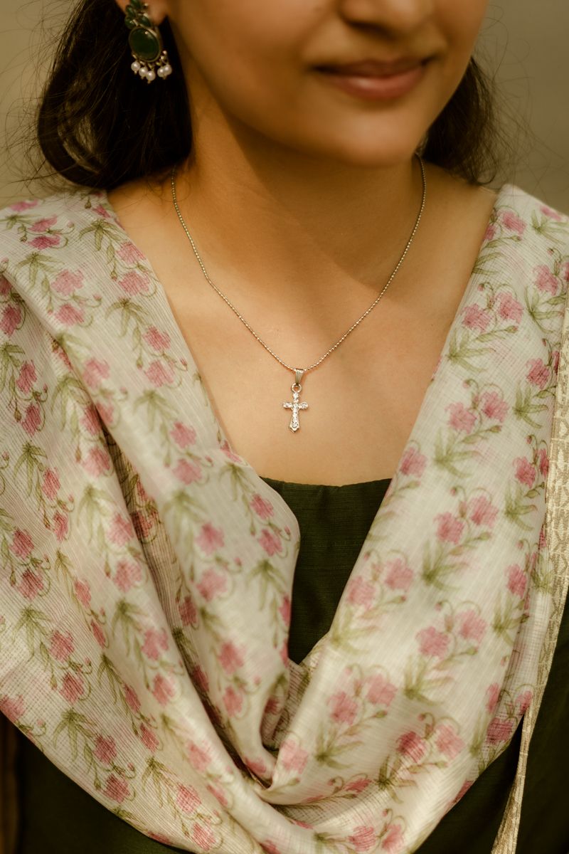 Close up of a delicate cross necklace and floral print dupatta against a black dress.