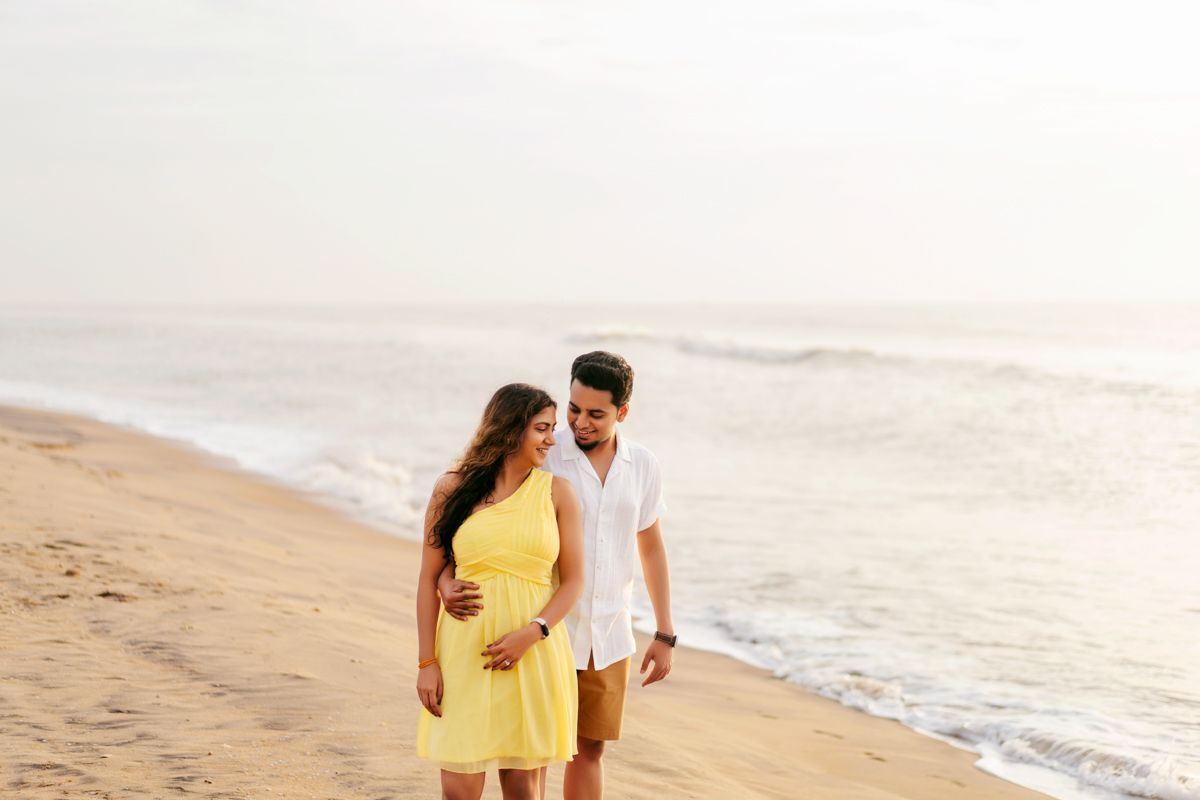 Couple walking together on sandy beach at sunset in coordinated white and yellow outfits.