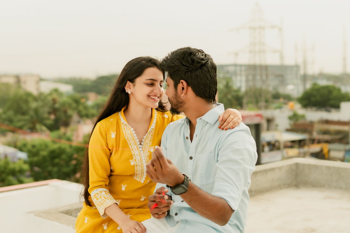 A couple shares an intimate moment on a rooftop terrace while wearing traditional yellow and white Indian attire.
