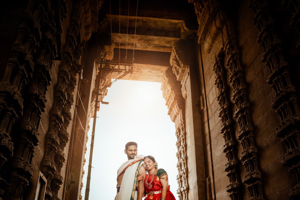 Couple in traditional Indian attire photographed through ornate temple doorway with dramatic lighting.