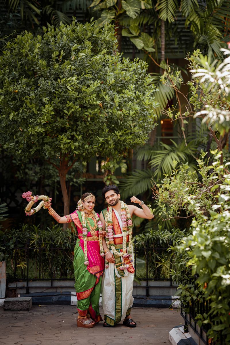 A couple in traditional Indian wedding attire pose joyfully in a lush garden setting.