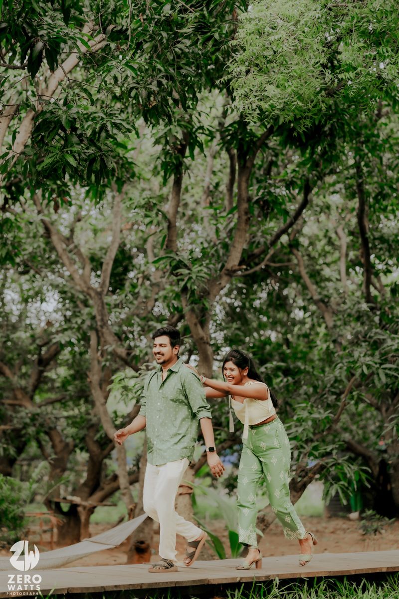 A couple dances joyfully on a wooden deck surrounded by lush green trees in a natural outdoor setting.