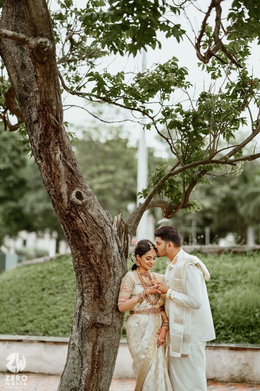 A romantic couple shares an intimate moment beneath a large tree in traditional South Asian wedding attire.