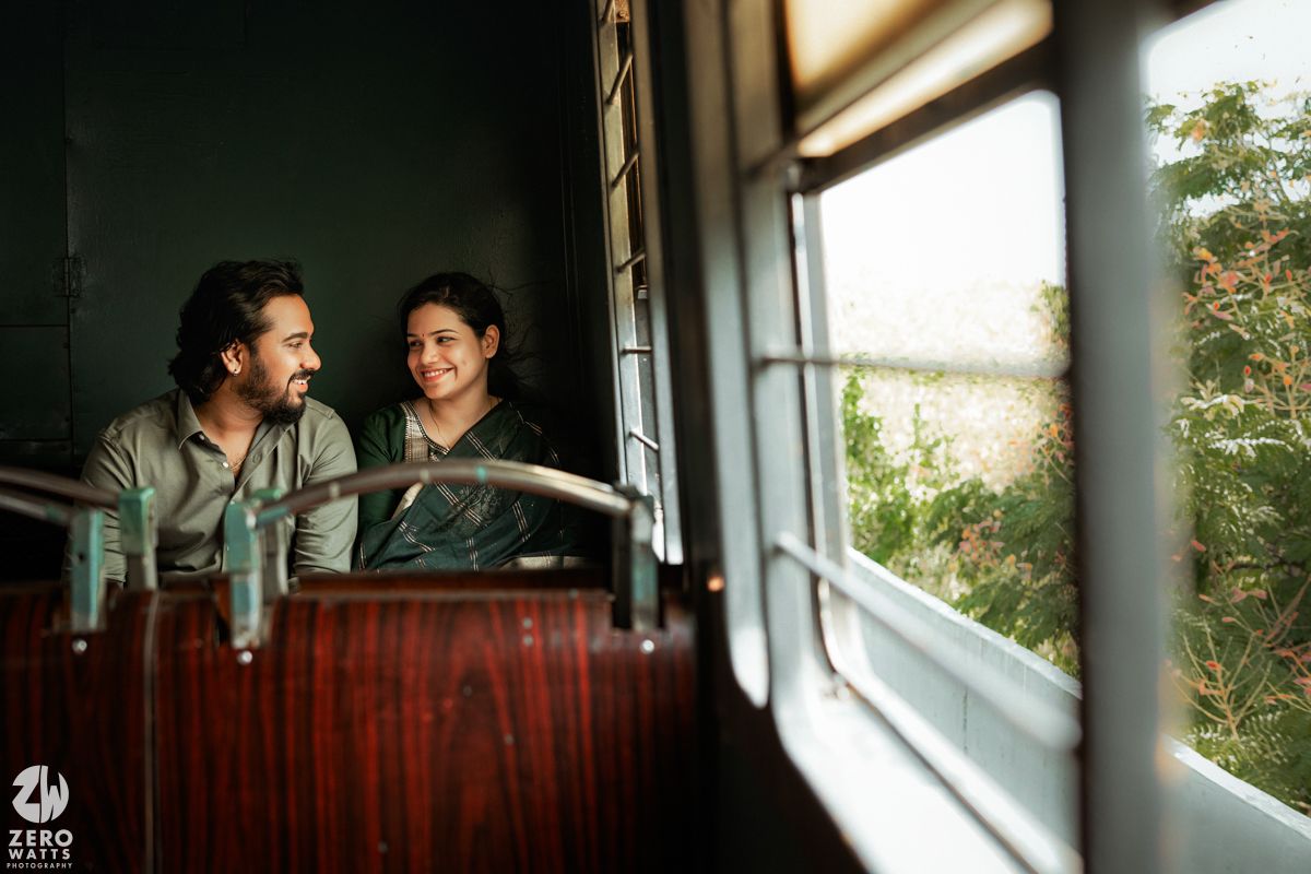 Two people share a joyful moment while riding on an old-fashioned train car looking out the window at scenic greenery.