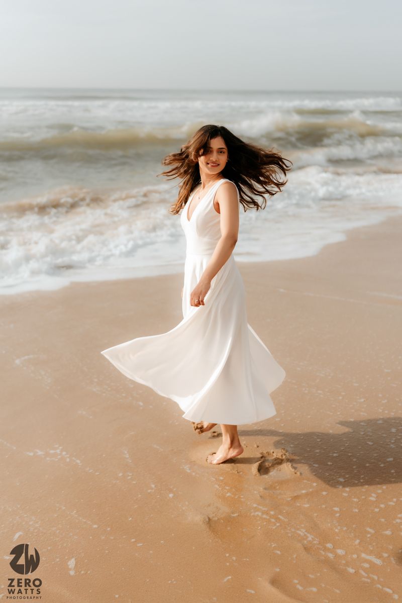 Woman in flowing white dress twirling on beach with wind-swept hair.