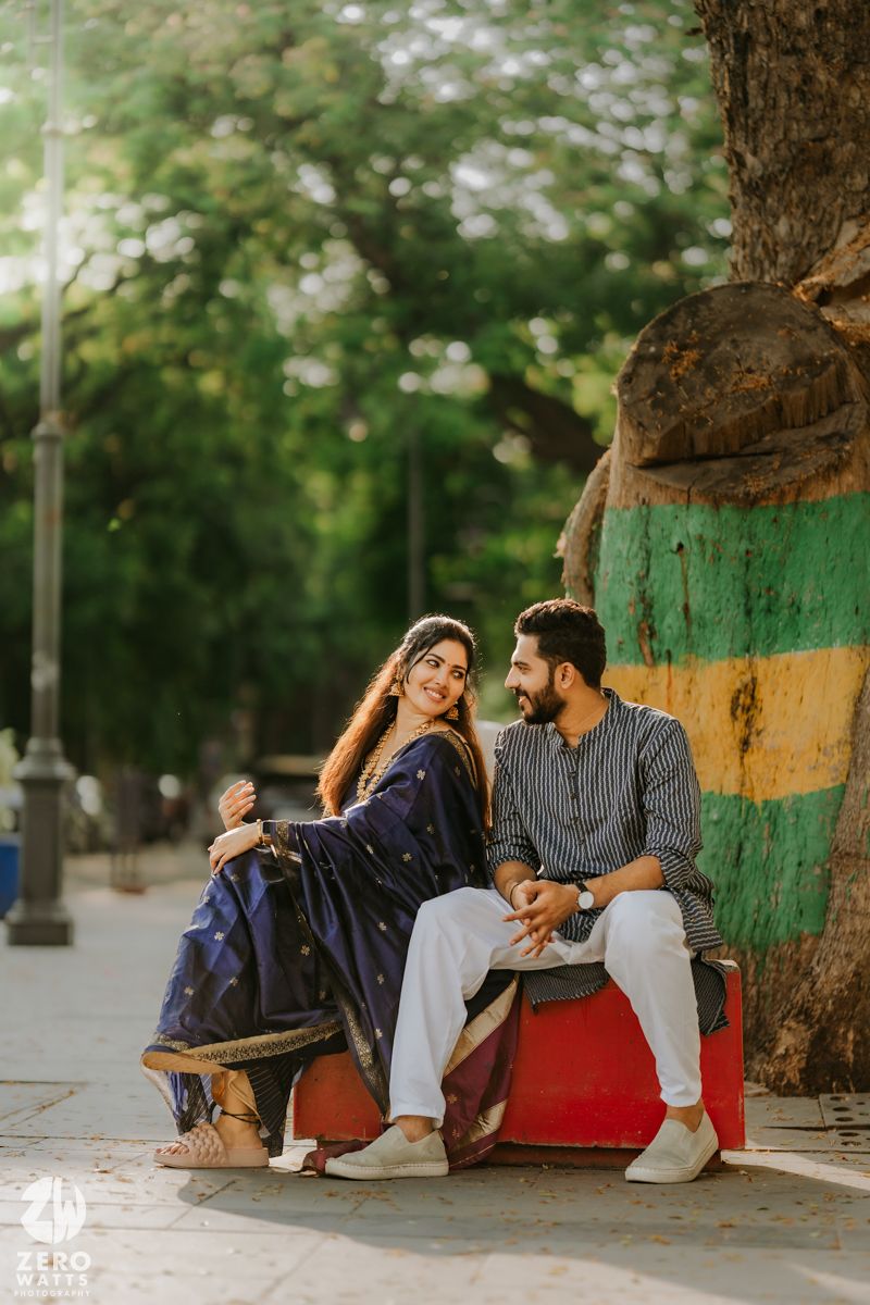 A couple sits together on colorful steps against a tree trunk in a park with soft bokeh background.