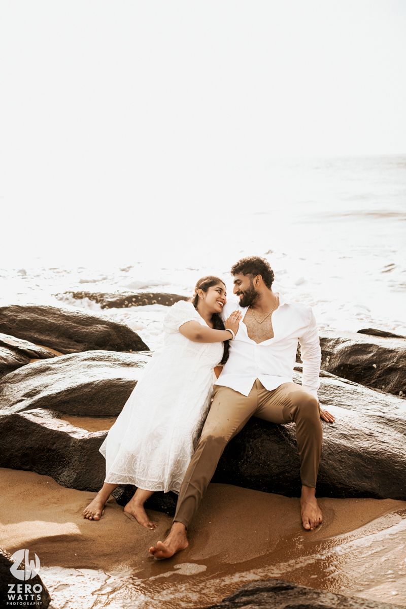 Couple relaxing on coastal rocks during sunset photoshoot.