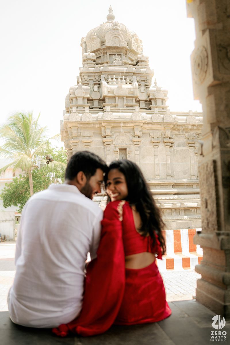 A couple sitting in traditional wear near an ancient South Indian temple with intricate architecture.