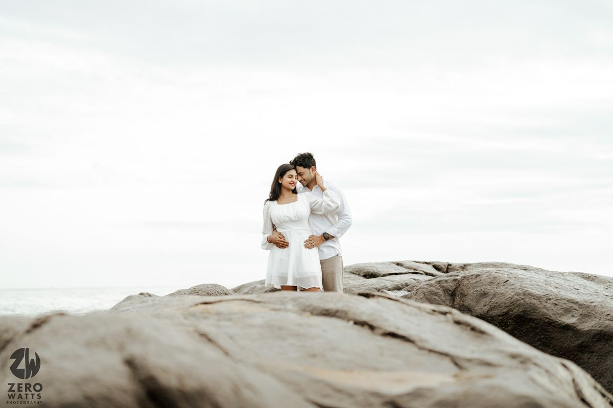 Two people stand close together on a rocky formation overlooking a scenic mountainous landscape at dusk.